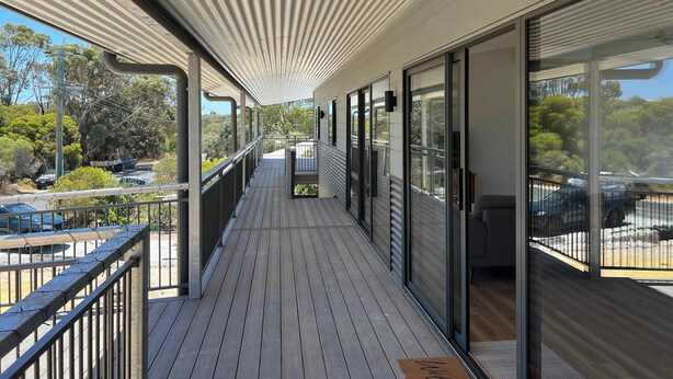 A covered balcony with a view of the surrounding area, including parked cars and trees.