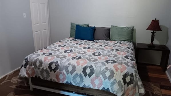 A bedroom with a bed, pillows, a nightstand, and a lamp.