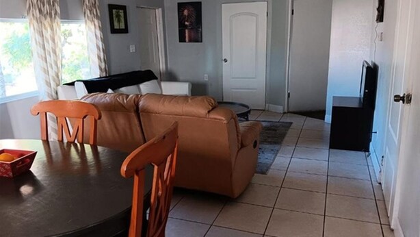 A living room with a brown sofa, a wooden dining table, and a TV stand. - GpL 3115 B 3 Bed 1 Bath (Fort Myers)