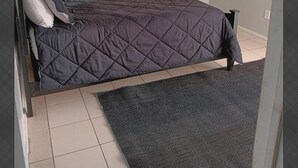 A bed with a quilted cover, a dark-colored rug, and a tiled floor. - GpL 3115 B 3 Bed 1 Bath (Fort Myers)