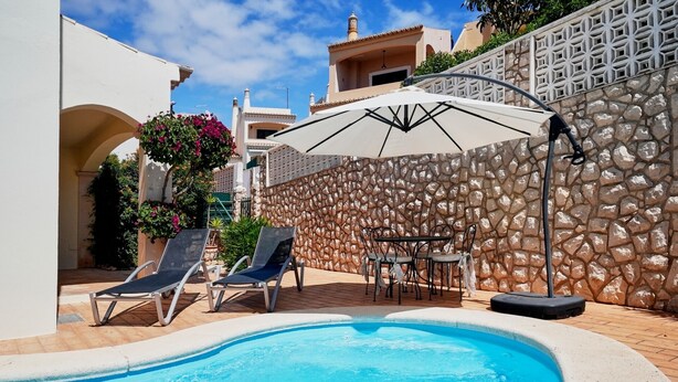 A swimming pool with lounge chairs and a table, surrounded by a stone wall and a white fence. - Villa sunset Solarenga is quiet villa w / private pool 10min from the beach (Lagoa)