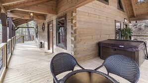 A wooden deck with two wicker chairs, a hot tub, and a wooden cabin structure. - Woodland Cabin: Hot Tub, Deck & Game Loft (Sevierville)