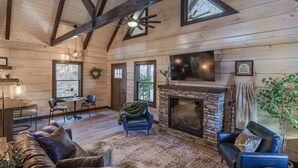 A wooden interior with a fireplace, leather sofas, a dining area, and a stone wall. - Woodland Cabin: Hot Tub, Deck & Game Loft (Sevierville)