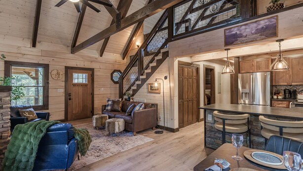 A spacious living area with a fireplace, a sofa, a coffee table, and a dining area with a table set for two. - Woodland Cabin: Hot Tub, Deck & Game Loft (Sevierville)