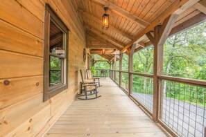 A wooden covered porch with rocking chairs, a railing, and a view of the forest. - Woodland Cabin: Hot Tub, Deck & Game Loft (Sevierville)