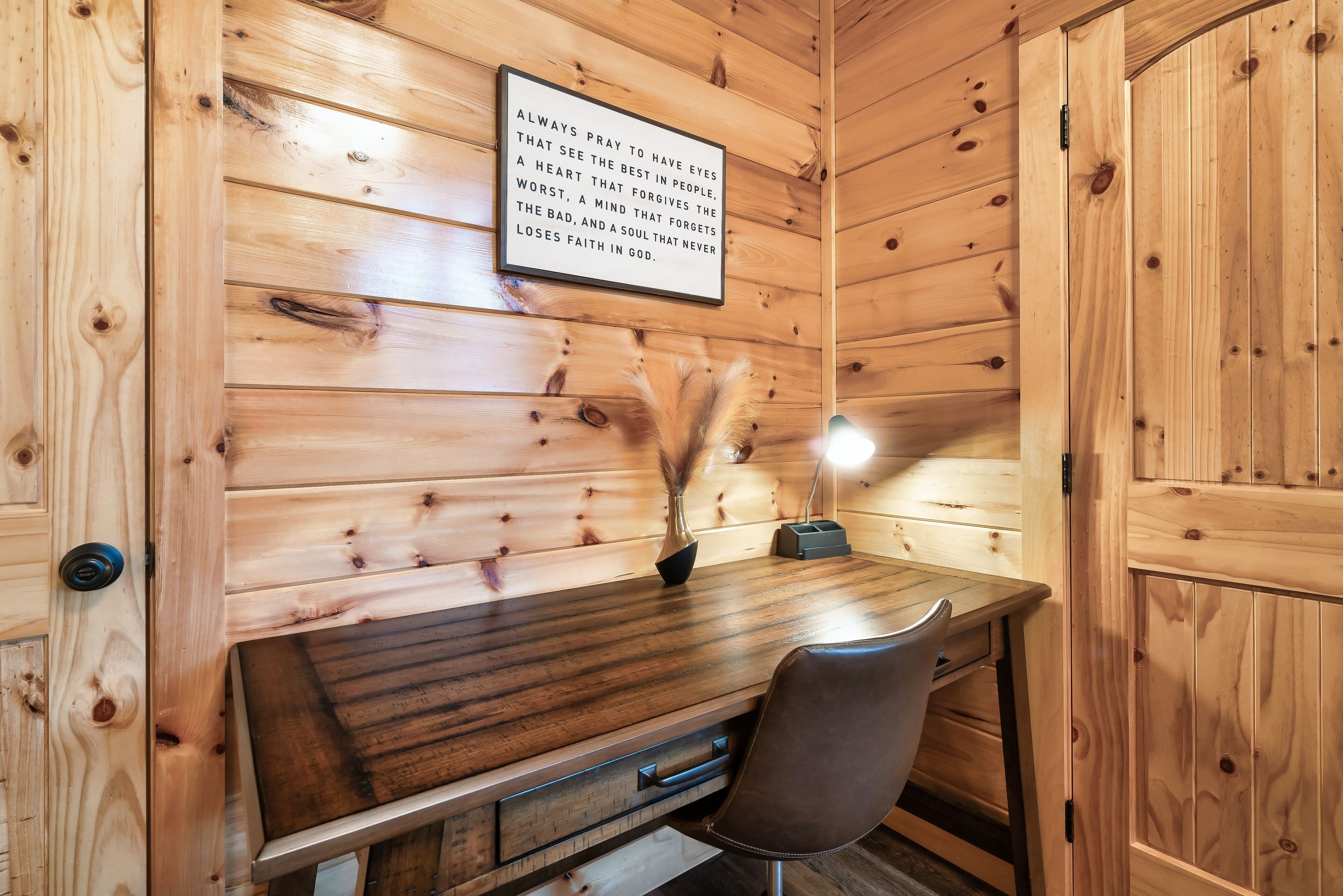 Ein Holzhütten-Interieur mit Schreibtisch, Stuhl und einem gerahmten Zitat an der Wand.