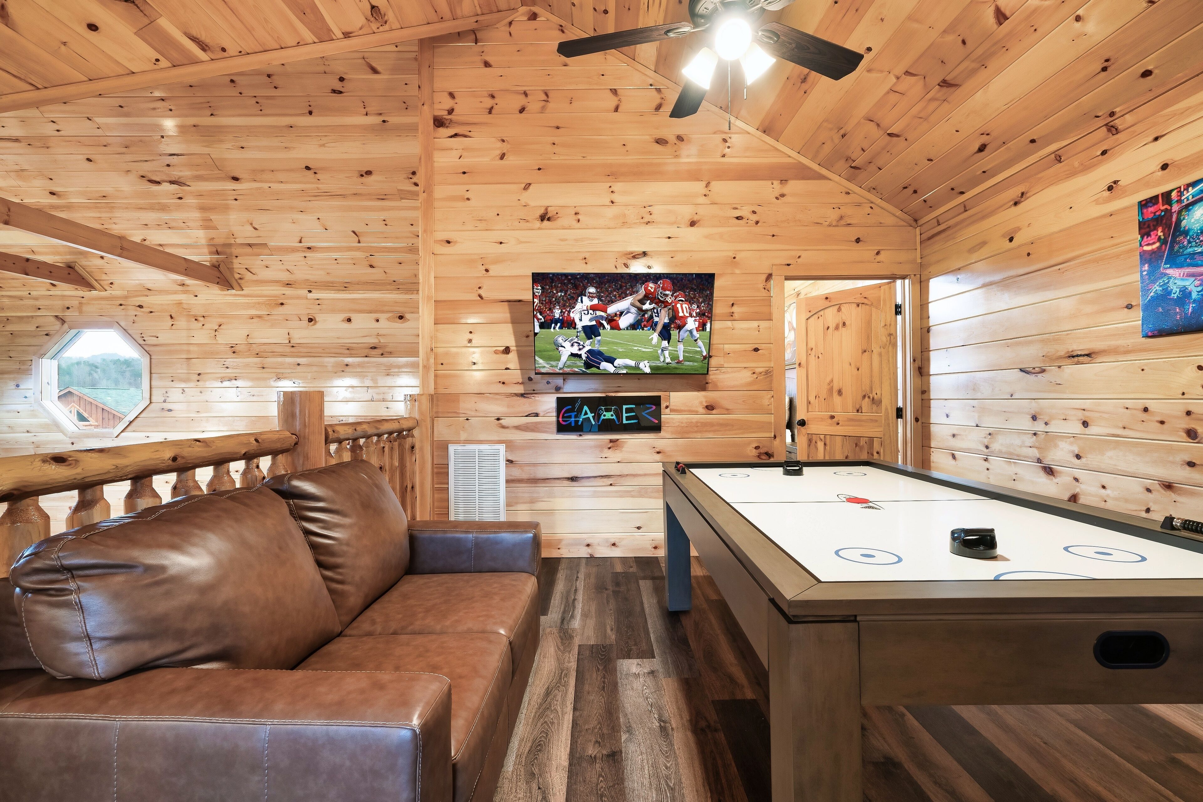 A wooden interior with a pool table, a brown leather sofa, and a mounted TV displaying a sports game.