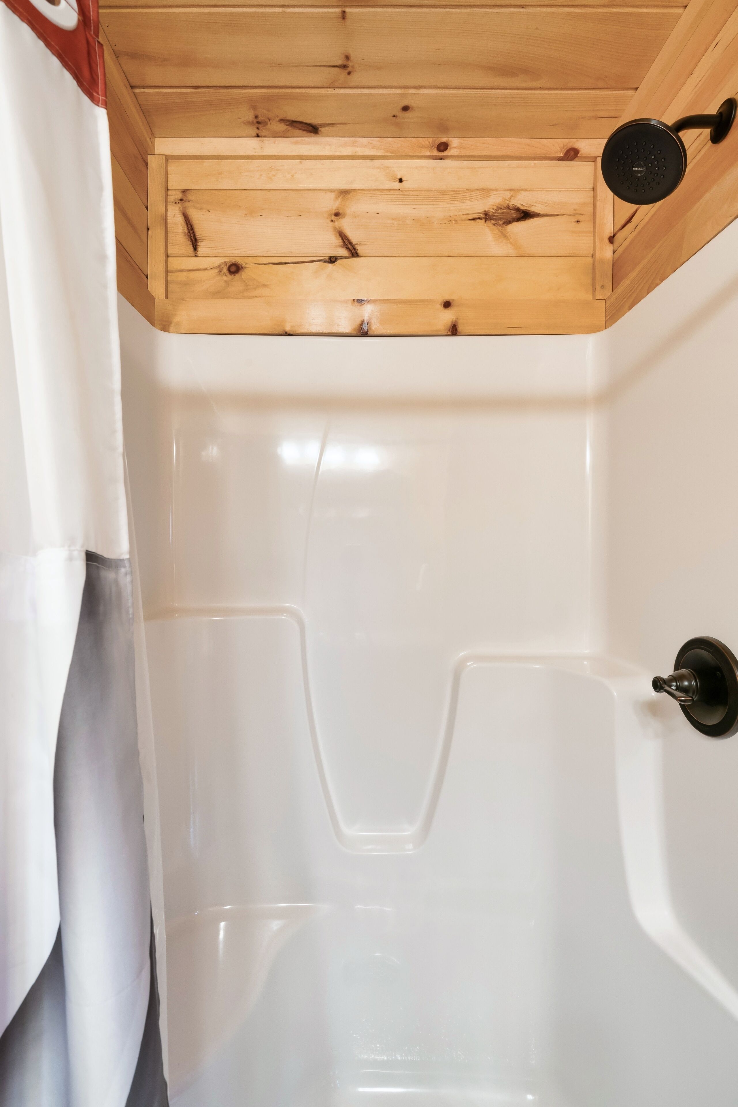 Un espace douche doté d’un plafond en bois et d’une baignoire blanche.