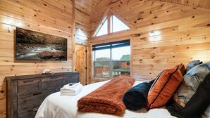 Ein Schlafzimmer einer Holzhütte mit einem Bett, einem Schminktisch, einem Gemälde und einem Fenster.