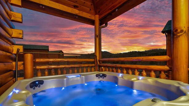 Ein Whirlpool mit digitaler Bedieneinheit, umgeben von Holzstämmen und einem Hollerdungszaun, mit Blick auf eine malerische Landschaft bei Sonnenuntergang.