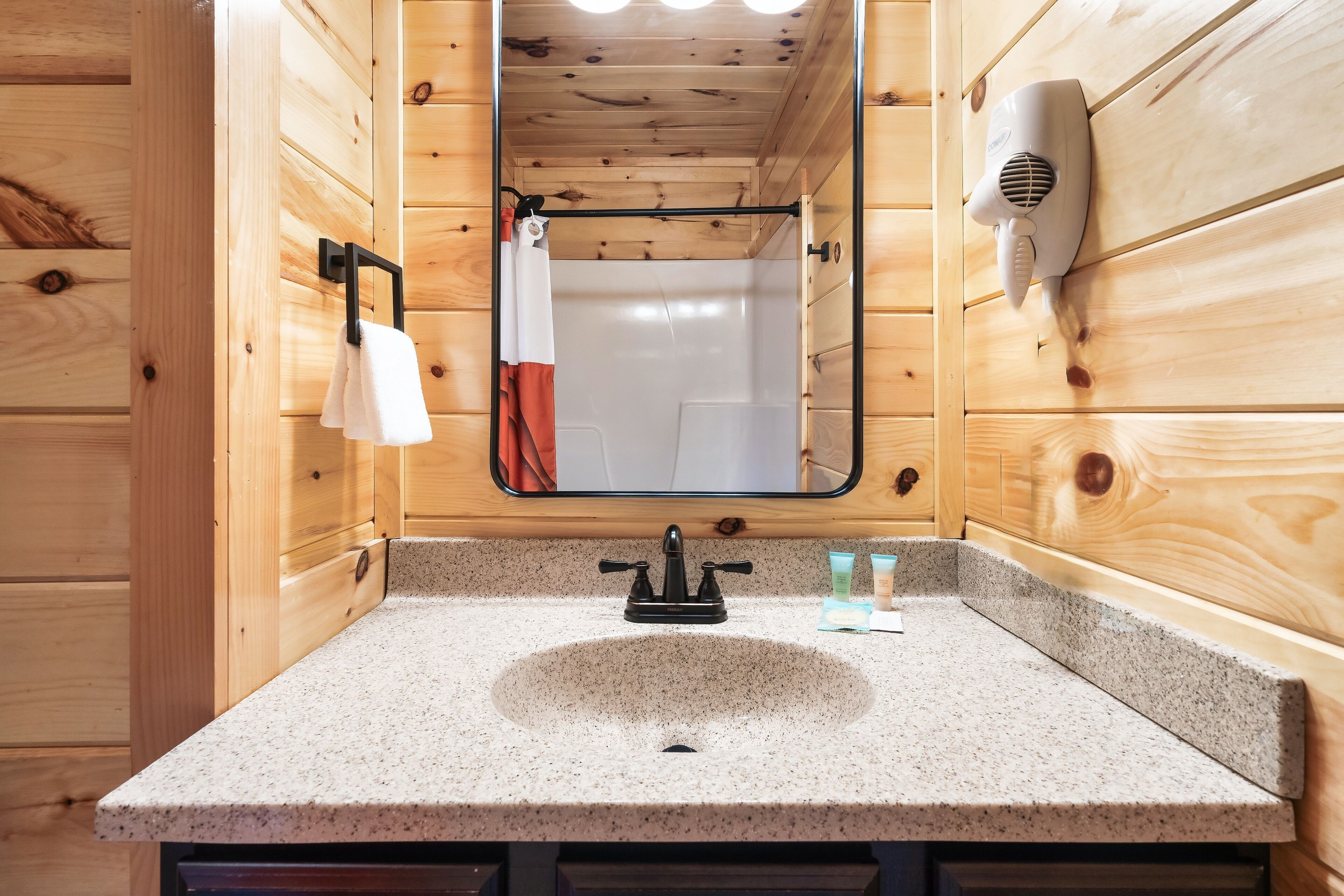 Une salle de bain avec des murs en bois, un lavabo en granit, un miroir, un porte-serviettes et un sèche-cheveux.
