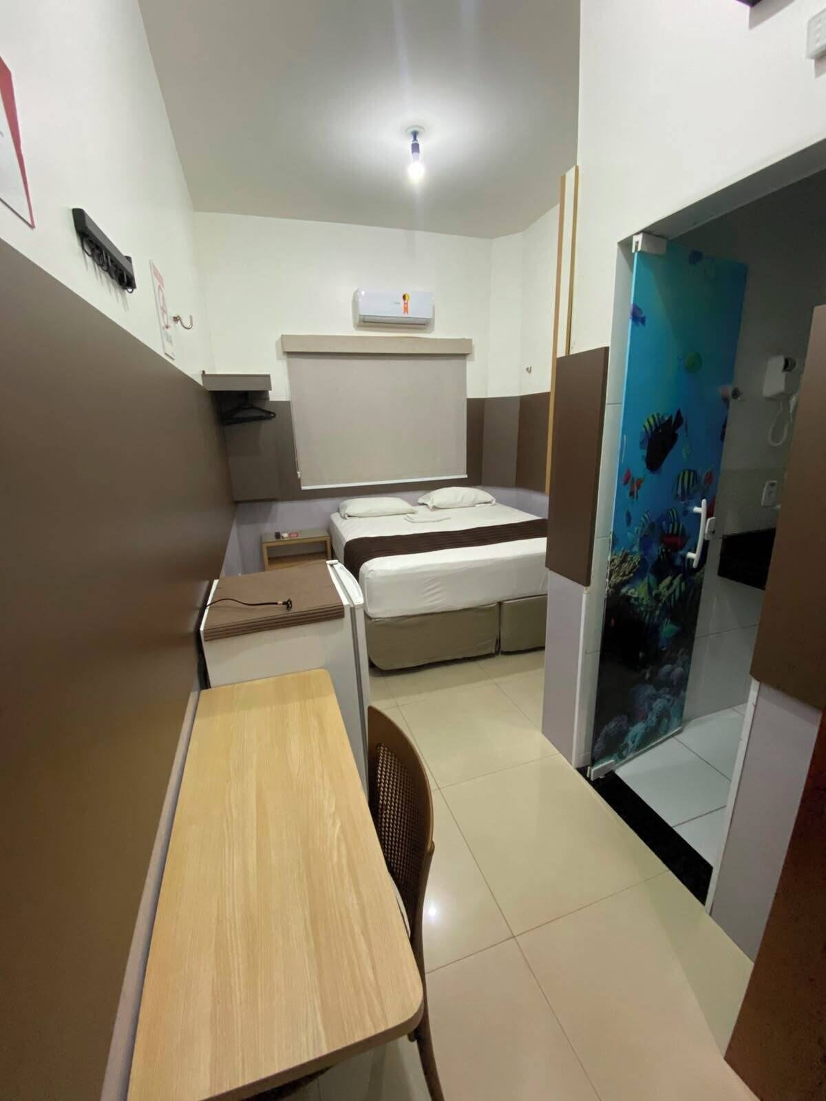 Habitación de hotel pequeña con cama, un escritorio, una silla y zona de ducha con un mural de peces.