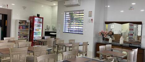 A dining area with tables and chairs, a refrigerator, and a window with blinds.