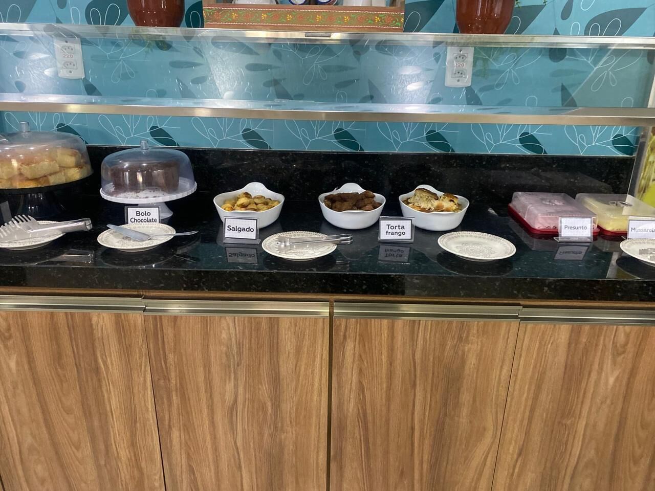 Een buffet met verschillende soorten eten, met labels in het Spaans, zoals chocolade, bolo, salgado, torta frango en presunto.