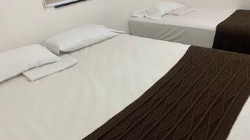 Habitación de hotel con dos camas, cada una con sábanas y almohadas blancas. Una cama tiene una manta marrón.