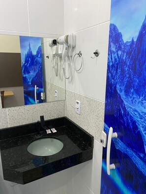 Un baño con lavamanos de mármol negro, paredes con azulejos blancos y un espejo.