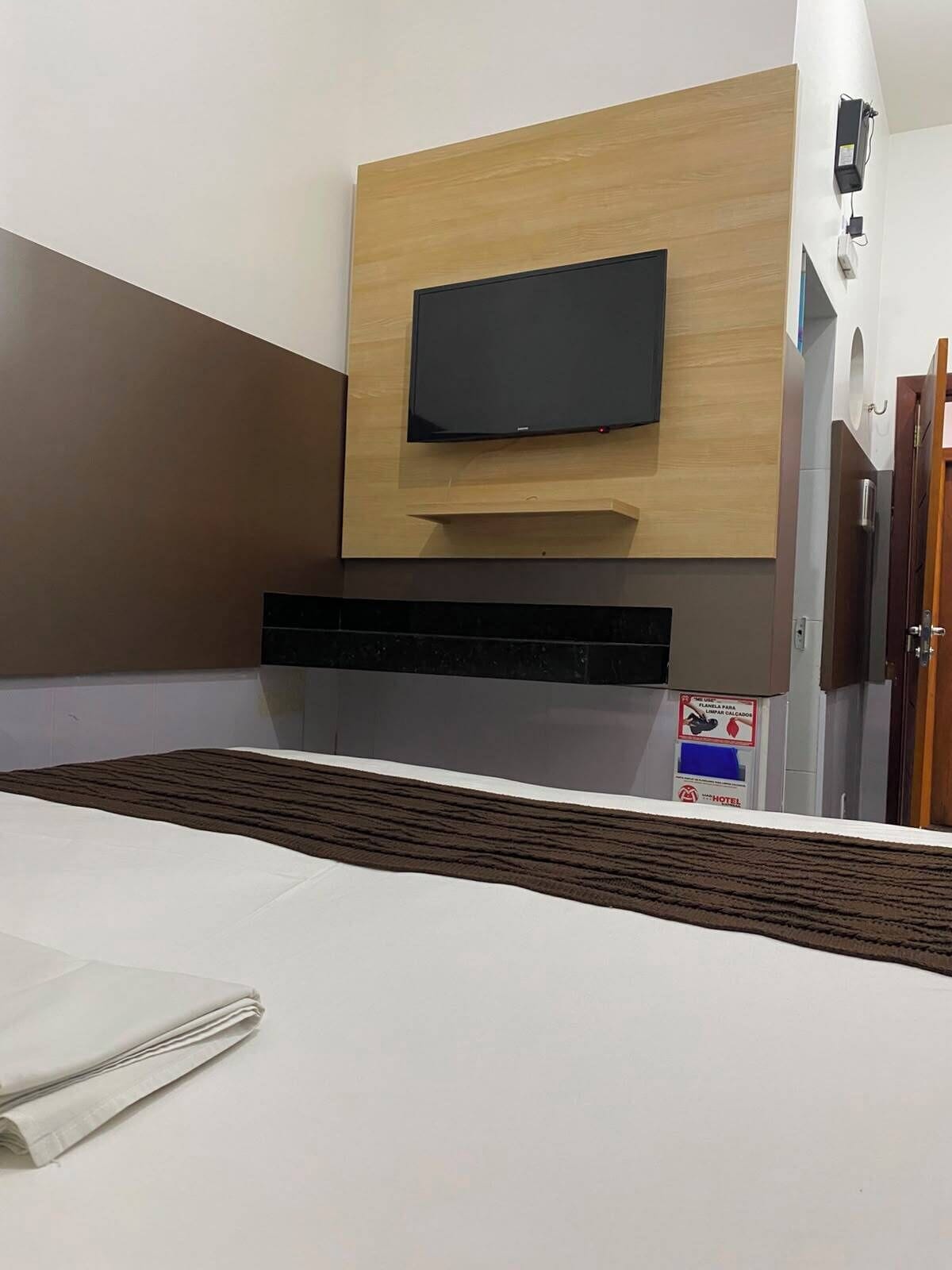 Habitación de hotel con televisión de pantalla plana montada sobre un panel de madera, cama con cubrecama a rayas blancas y marrones, y un letrero que indica que la habitación es de uso exclusivo para huéspedes.