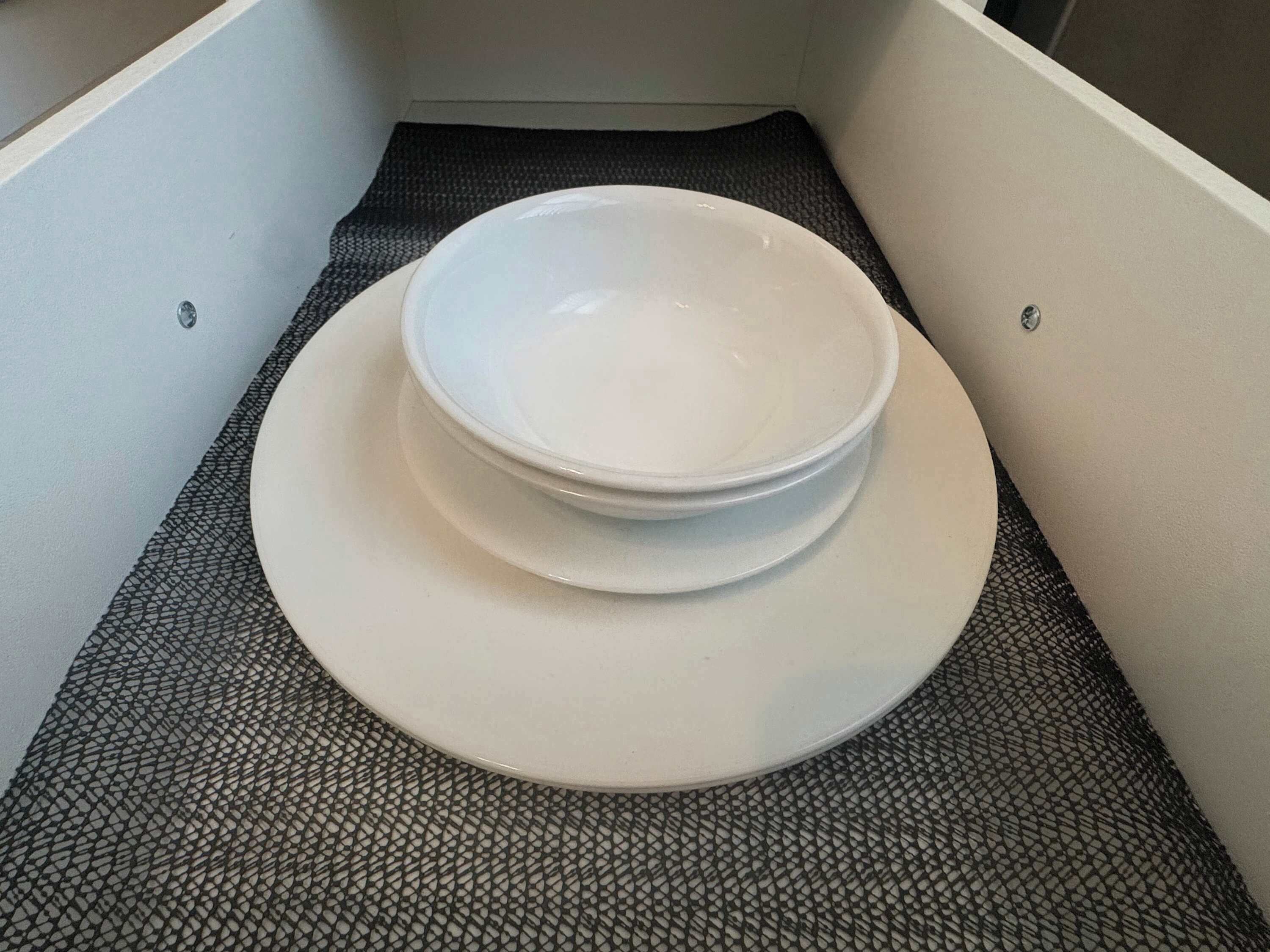 A white bowl on a textured mat in a corner of a room.