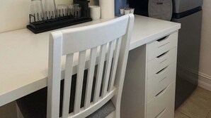 Una kitchenette compacta con encimera blanca, microondas, refrigerador y una silla.