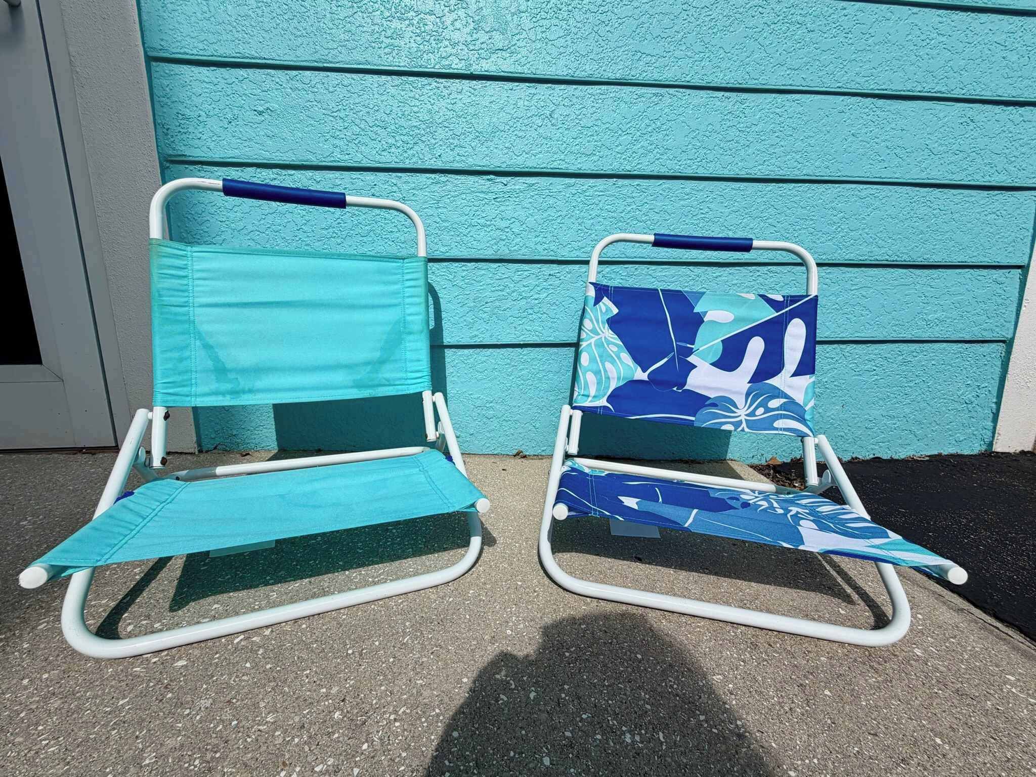 Two beach chairs with fabric covers, positioned on a concrete surface against a teal-painted wall.