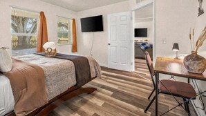Une chambre à coucher comprenant un lit, un bureau, une chaise, un téléviseur et une porte donnant sur une autre pièce.