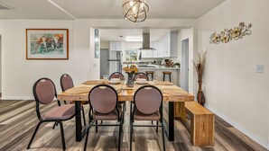Un coin repas avec une table en bois, six chaises, un vase de fleurs et un lustre.