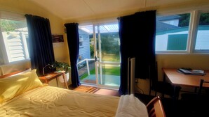A hotel room with a bed, a desk, a chair, and a sliding glass door leading to a balcony.