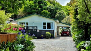 A single-story house with a covered garage, surrounded by lush greenery and flowering plants.
