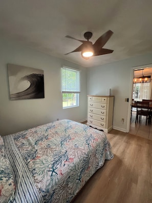Une chambre à coucher comprenant un lit, une commode, un ventilateur de plafond, une fenêtre et une porte donnant sur un coin repas.