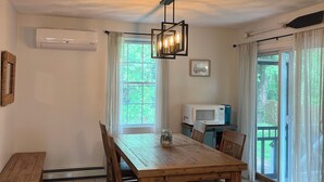 Ein Essbereich mit einem Holztisch, Stühlen, einer Chandelier, einer Mikrowelle und Blick durch die Fenster.