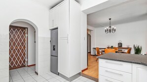 Une cuisine moderne avec des meubles blancs, un réfrigérateur gris et un coin repas en bois avec des chaises orange.
