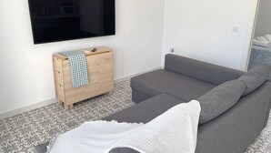 Ein modernes Wohnzimmer mit einem grauen Sofa, einem Holzschrank mit kariertem Tuch und einem flachbildfernseher an der Wand.