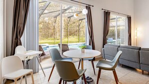 Ein modernes Wohnzimmer mit Blick auf einen Pool, einem Essbereich mit Stühlen und einem Tisch sowie einem grauen Sofa.
