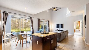 Eine moderne Küche mit Kochinsel, Essbereich mit Stühlen, einer Couch und einem Fernseher.