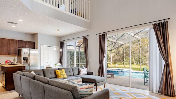 Ein geräumiger Wohnbereich mit grauem Ecksofa, einer Küche mit dunklen Holzschränken und einer großen Glasschiebetür, die zu einem Pool führt.