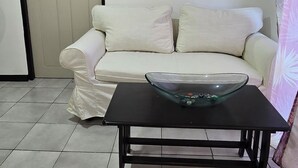 Un saló amb un sofà blanc, una taula de cafè negra amb un bol de vidre i un mirall a la paret.