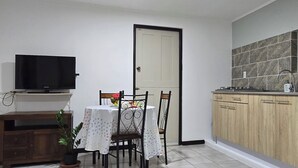 Una cuina compacta amb zona de menjador, un televisor sobre un moble i una porta que condueix a una altra habitació.