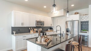 A modern kitchen with white cabinets, stainless steel appliances, a central island, and bar stools. - Modern cozy 4-bedroom house in pleasant Grand Junction (Grand Junction)