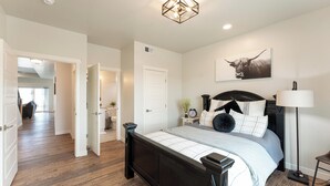 A bedroom with a large bed, a bedside table with a lamp, and a wall-mounted artwork. - Modern cozy 4-bedroom house in pleasant Grand Junction (Grand Junction)