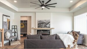 A modern living room with a fireplace, a ceiling fan, and a large window. - Modern cozy 4-bedroom house in pleasant Grand Junction (Grand Junction)