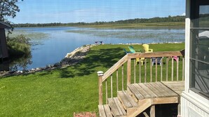 En terrass med ett träräcke som vetter mot en sjö, ett gräsområde och ett litet förråd.