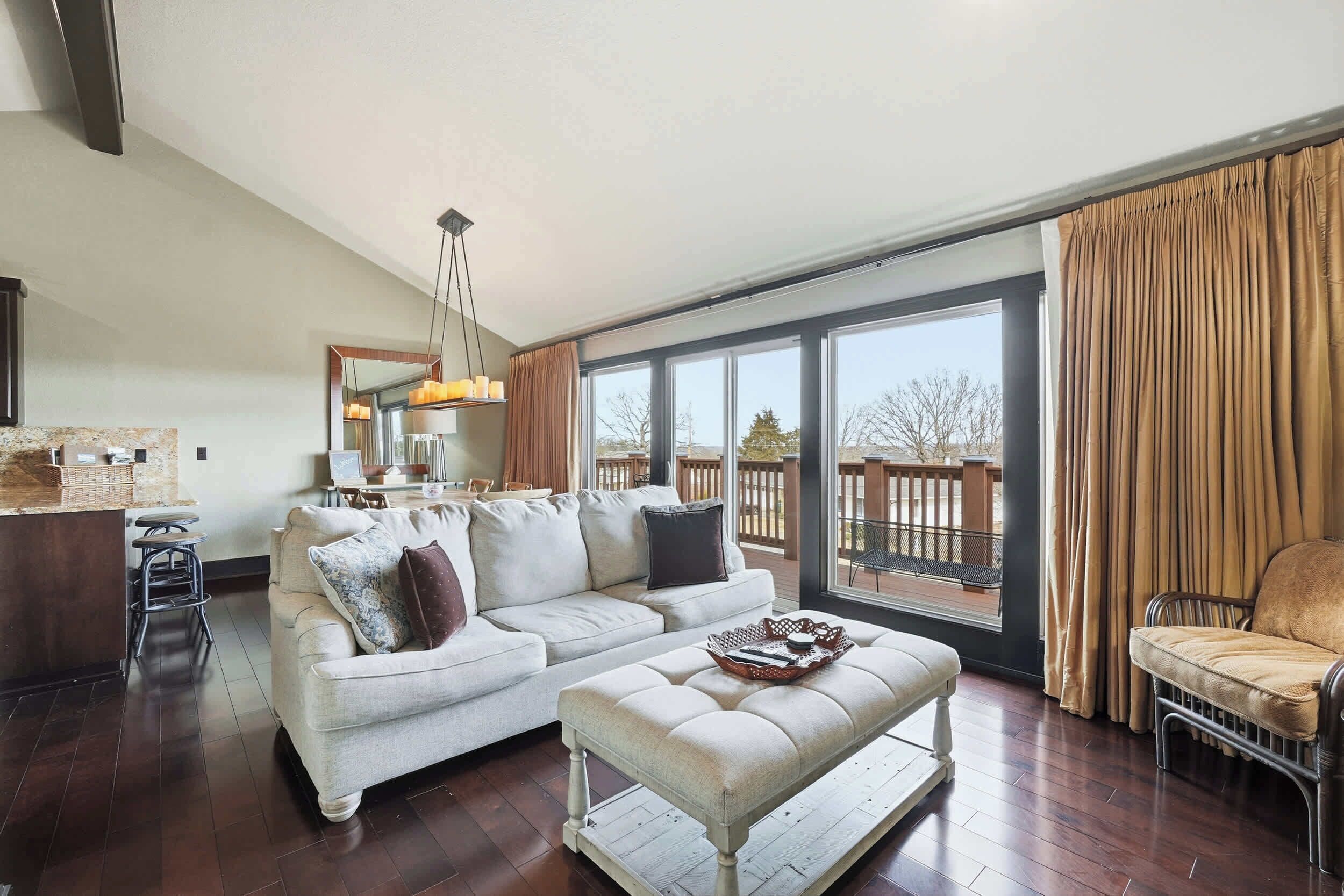 A spacious living room with a large window, a sofa, an ottoman, and a chair.