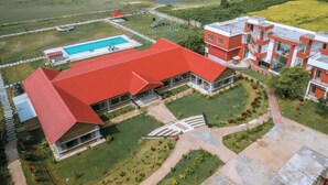 Vista aerea di un edificio moderno con tetto rosso, circondato da giardini curati e una piscina.