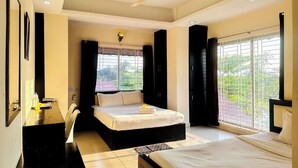 Una camera d'albergo con un letto, una scrivania, una sedia, una ventola a soffitto e ampie finestre.