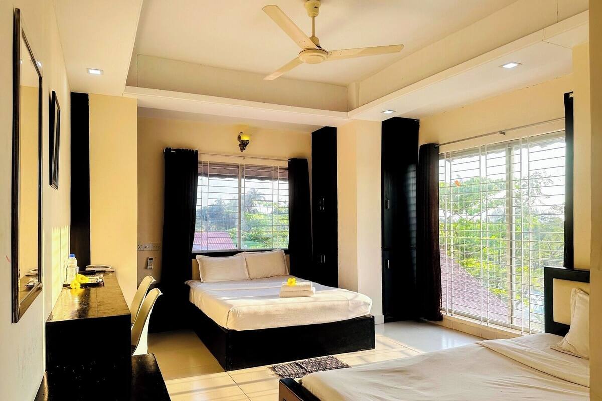 Une chambre d’hôtel équipée d’un lit, d’un bureau, d’une chaise, d’un ventilateur de plafond et de grandes fenêtres.