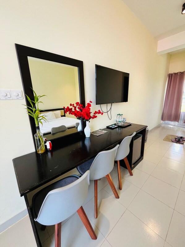 Une chambre d’hôtel moderne avec une table à manger noire, des chaises blanches, un grand miroir, un téléviseur à écran plat et une plante en pot.