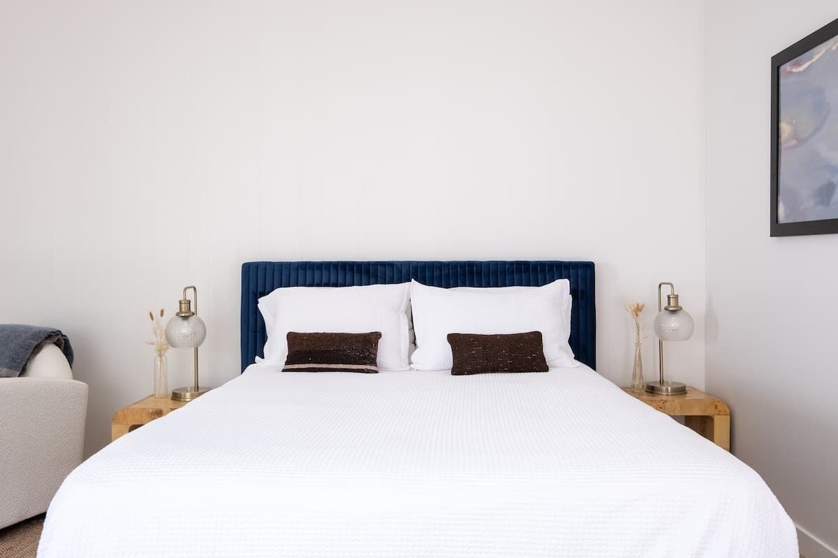 A neatly made bed with white bedding and two dark brown pillows, flanked by wooden nightstands with lamps.