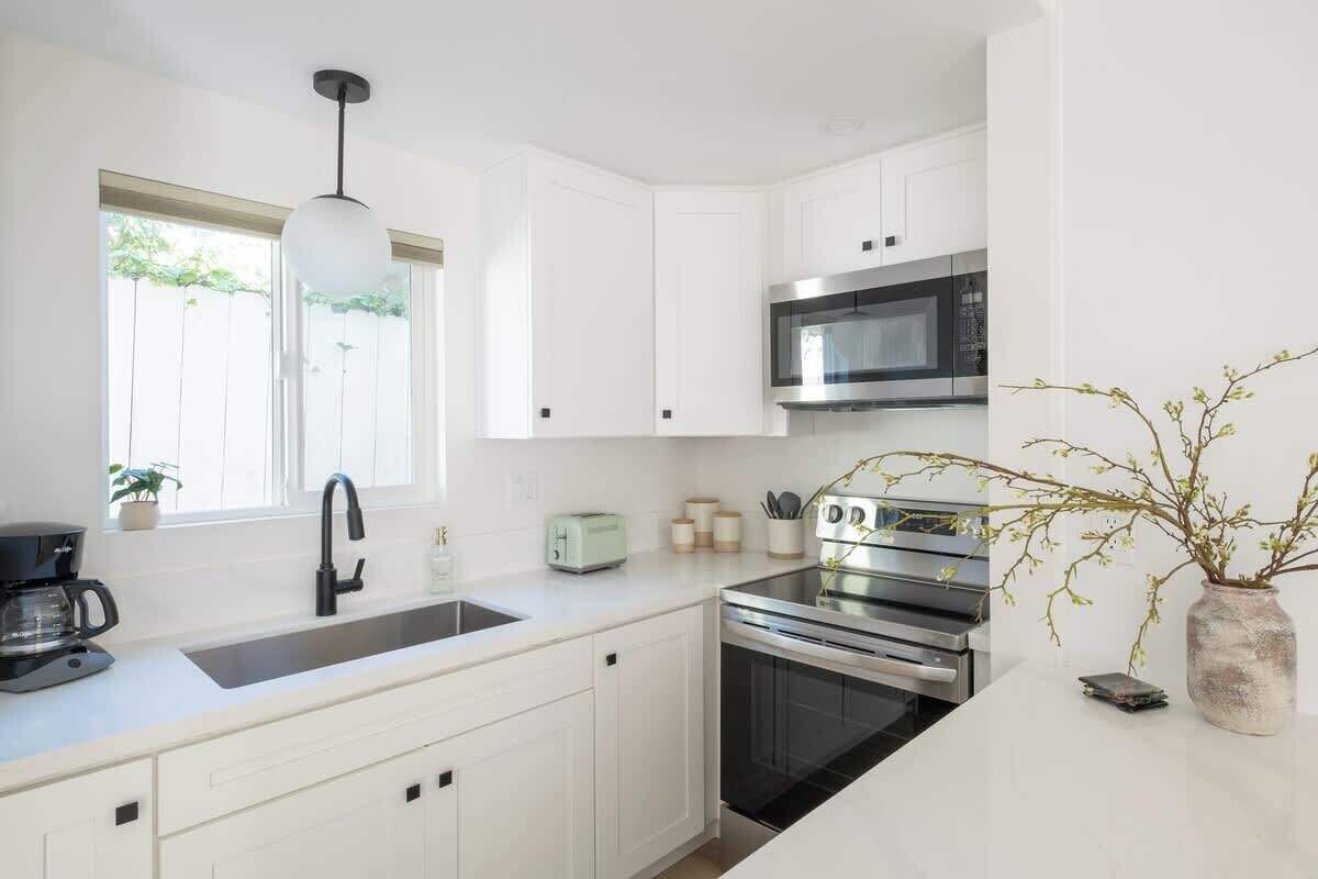 Een moderne keuken met witte kasten, een roestvrijstalen oven, een magnetron en een koffiezetapparaat.