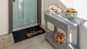Una entrada moderna con una puerta de vidrio satinado, un felpudo, una mesita con adornos y un aplique de techo.