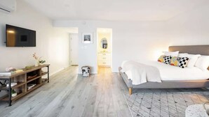 Un dormitorio moderno con una cama, un televisor montado en la pared, un escritorio de madera y una mesita con objetos decorativos.